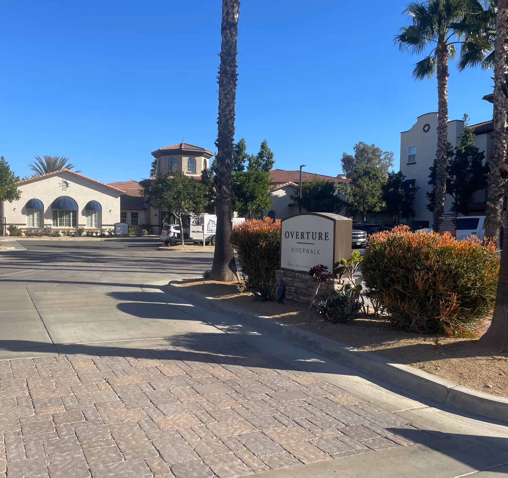 Exterior view of Overture Riverwalk showing the entrance sign, palm trees, landscaping, and the building facade.