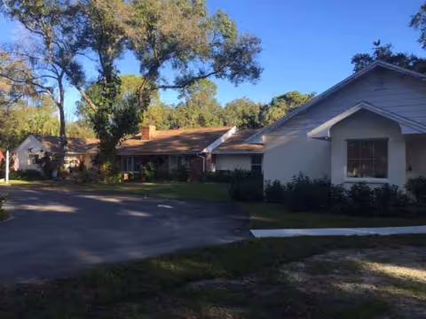 Exterior view of A Country Place Assisted Living Facility with trees and driveway.