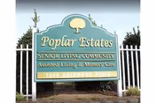 Green entrance sign reading "Poplar Estates Senior Living Community, Assisted Living & Memory Care" mounted between white posts with trees behind it.