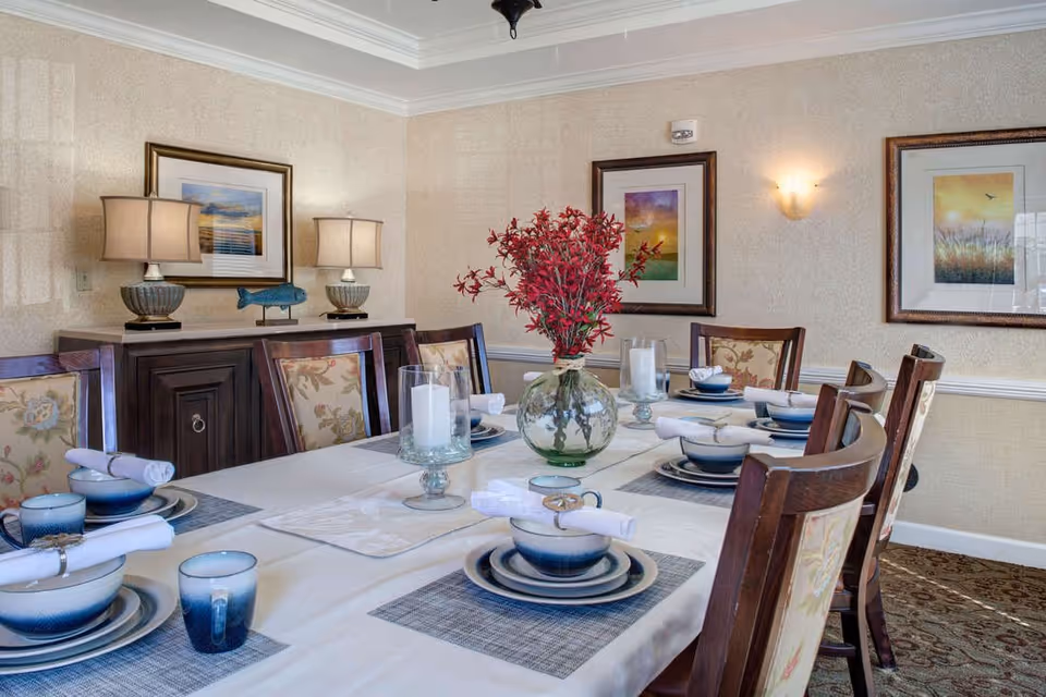 Elegantly set dining table with blue-and-white place settings, a glass vase of red flowers, and framed artwork in a softly lit dining room.