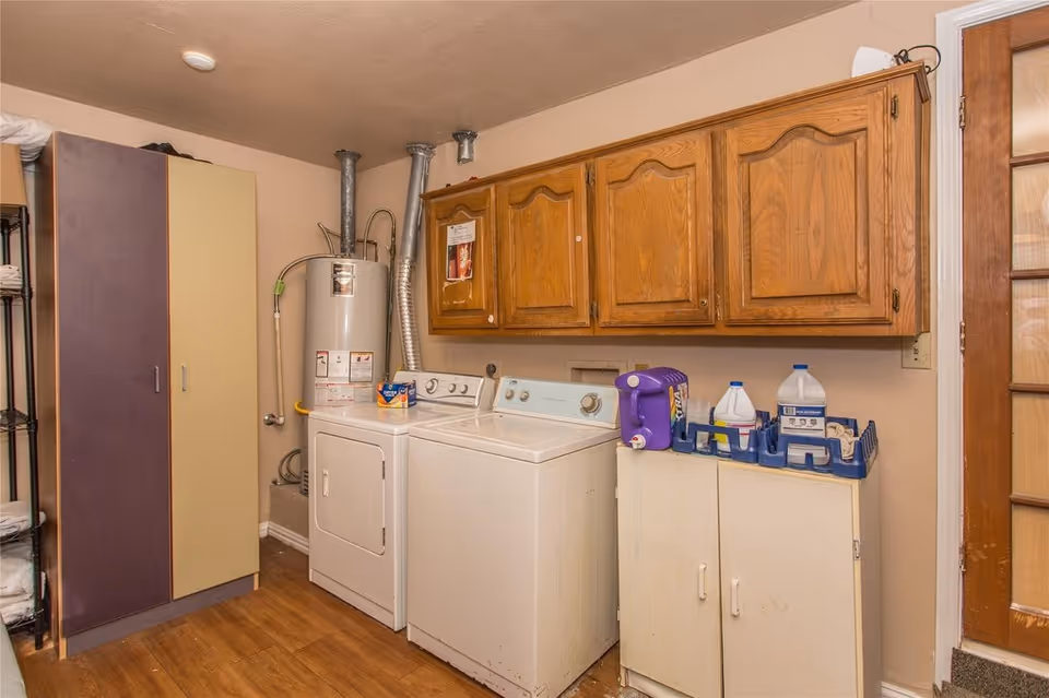 Laundry room with a washer and dryer, water heater, wooden wall cabinets, and storage cupboards.