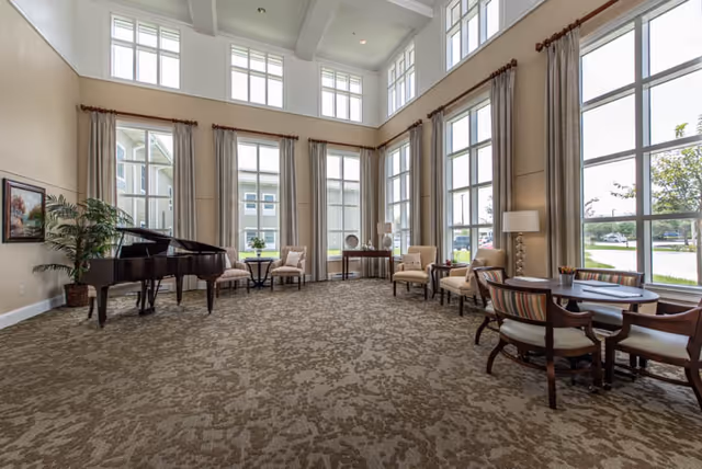 Spacious two-story common room with tall windows, a grand piano, seating areas, and tables.