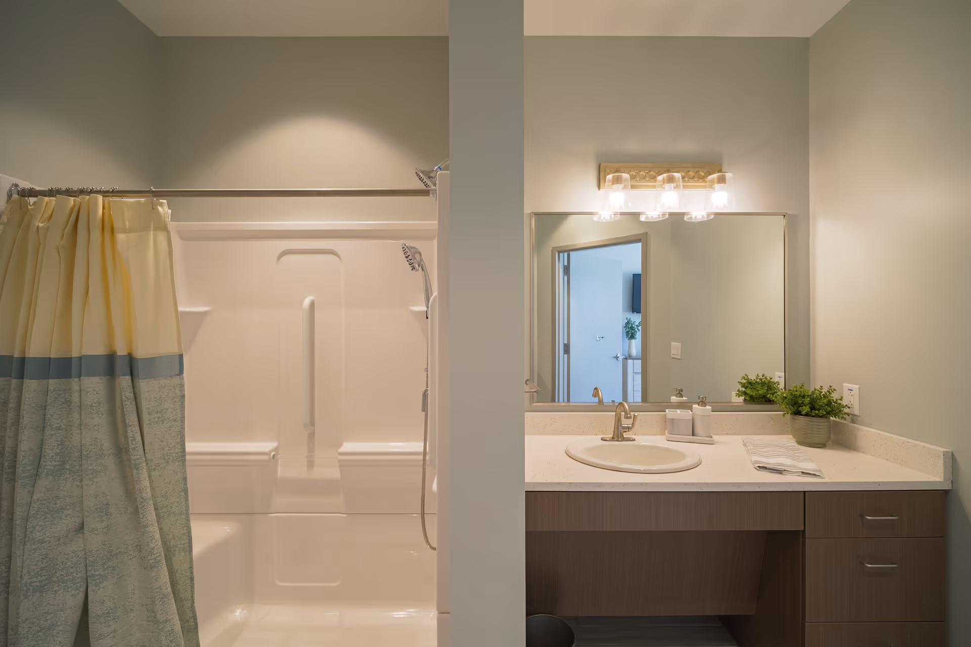 A clean, modern bathroom showing a shower with a curtain on the left and a vanity with sink, mirror, and light fixture on the right.