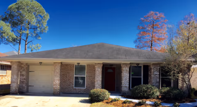 Single-story brick senior residence exterior with a dark roof, red front door, and shrubs.