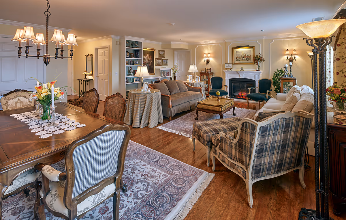 Spacious, elegantly furnished open living and dining area with sofas, armchairs, a fireplace, and a dining table under a chandelier.