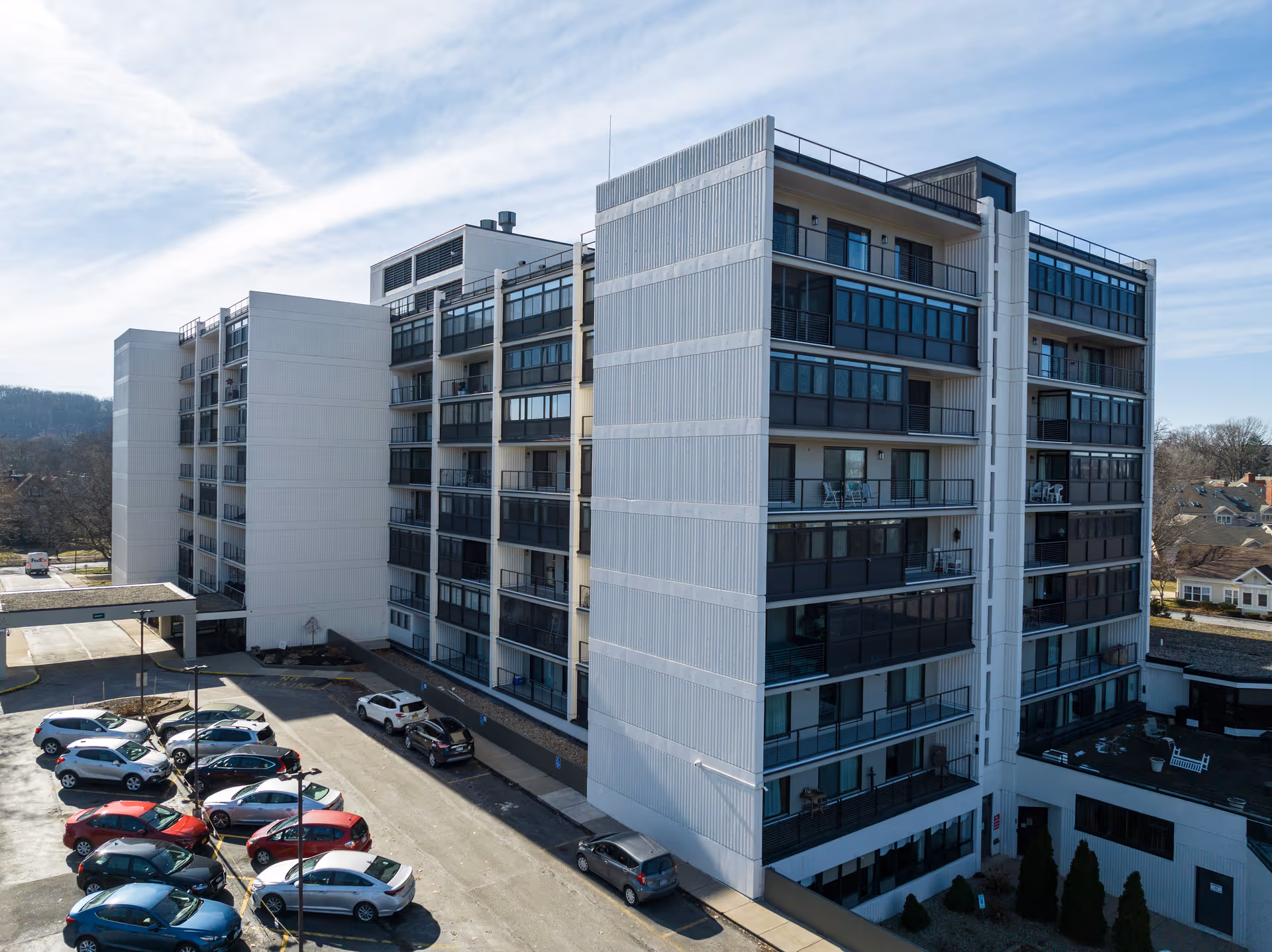 Exterior view of a multi-story assisted living building with balconies, parked cars, and a driveway.