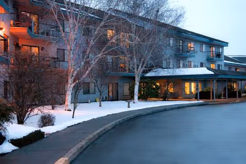 Snowy exterior of Evergreen Estates senior living building with lit windows and bare trees.