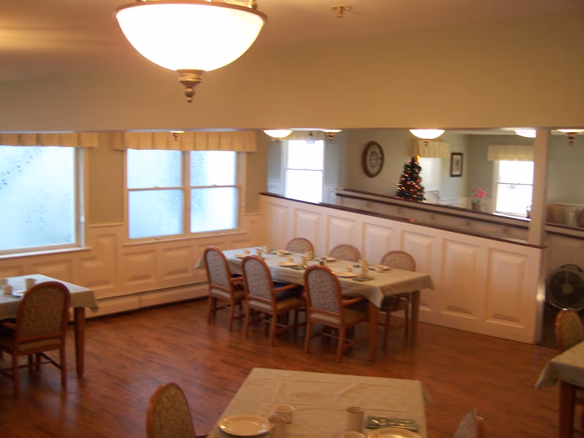 Dining room with several set tables and chairs, hardwood floors, and a small decorated Christmas tree.