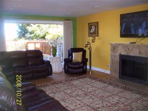Living room in a senior care facility with leather seating, yellow walls, fireplace, and outdoor view.