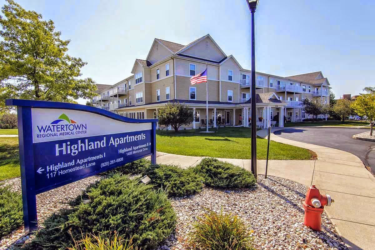 Exterior view of the Highland Apartments building with a foreground sign, flagpole, and landscaped entrance.