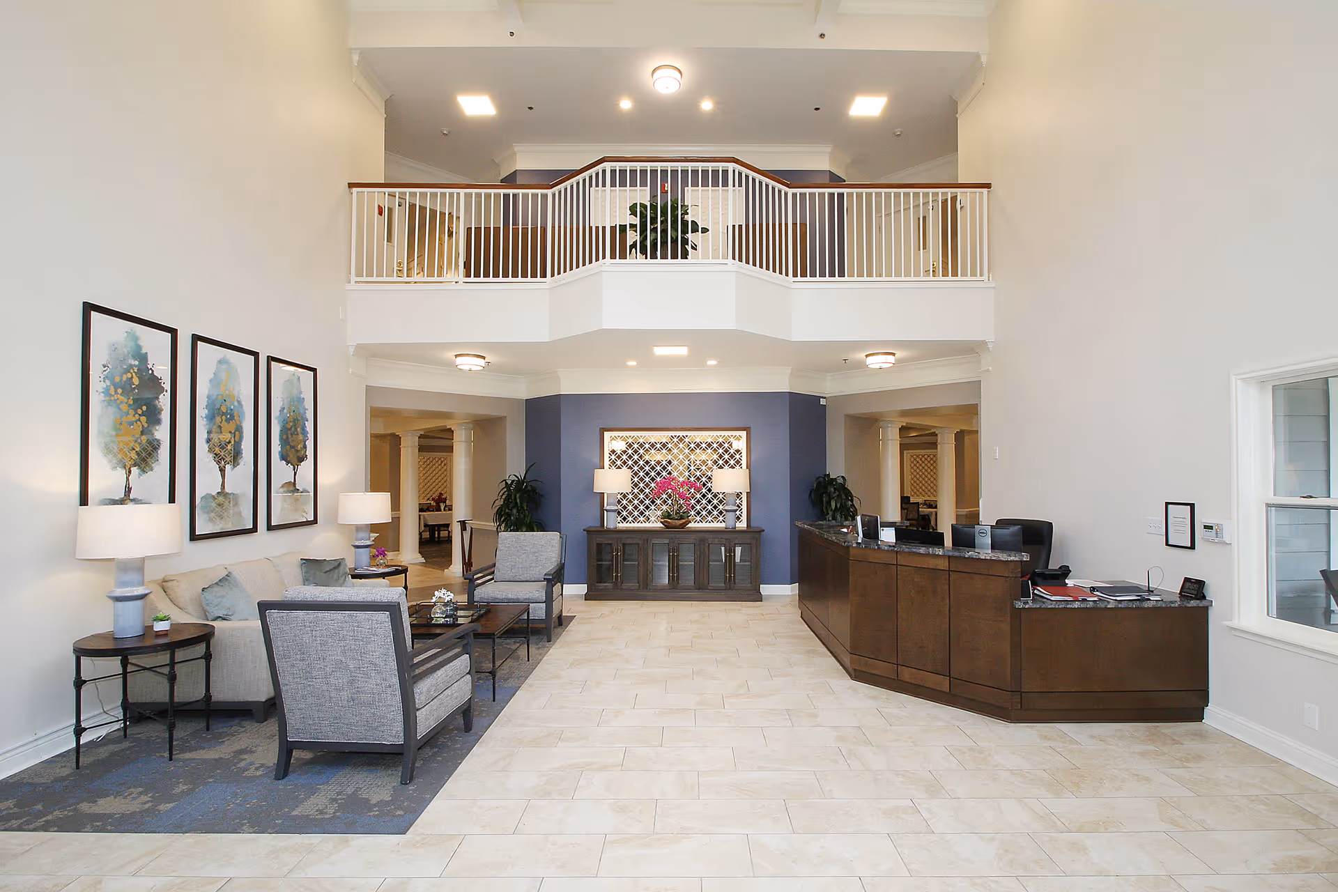 Spacious senior living lobby with seating area, reception desk, and a second-floor balcony overlooking the space.