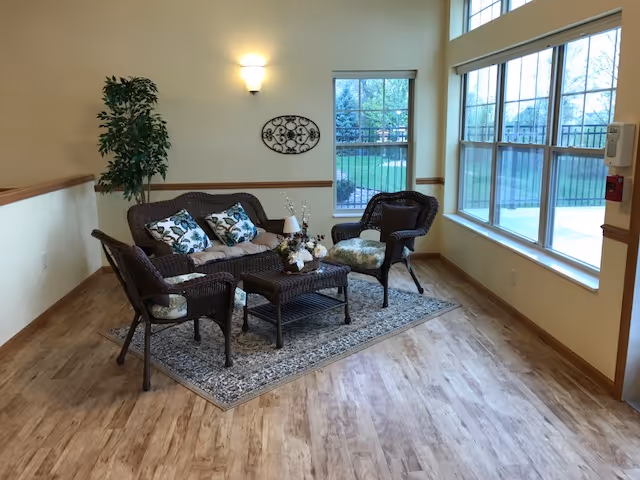 A cozy wicker seating area with coffee table and large windows in a senior living lounge.