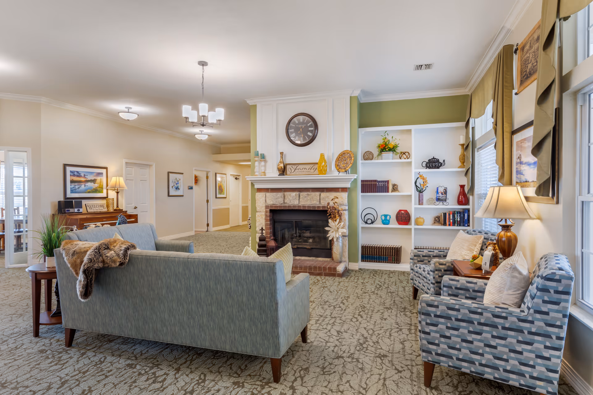 Bright, cozy common living room with sofas and armchairs arranged around a fireplace and built-in shelving.