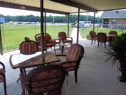 Outdoor covered patio with red-striped cushioned chairs and tables overlooking a grassy area.