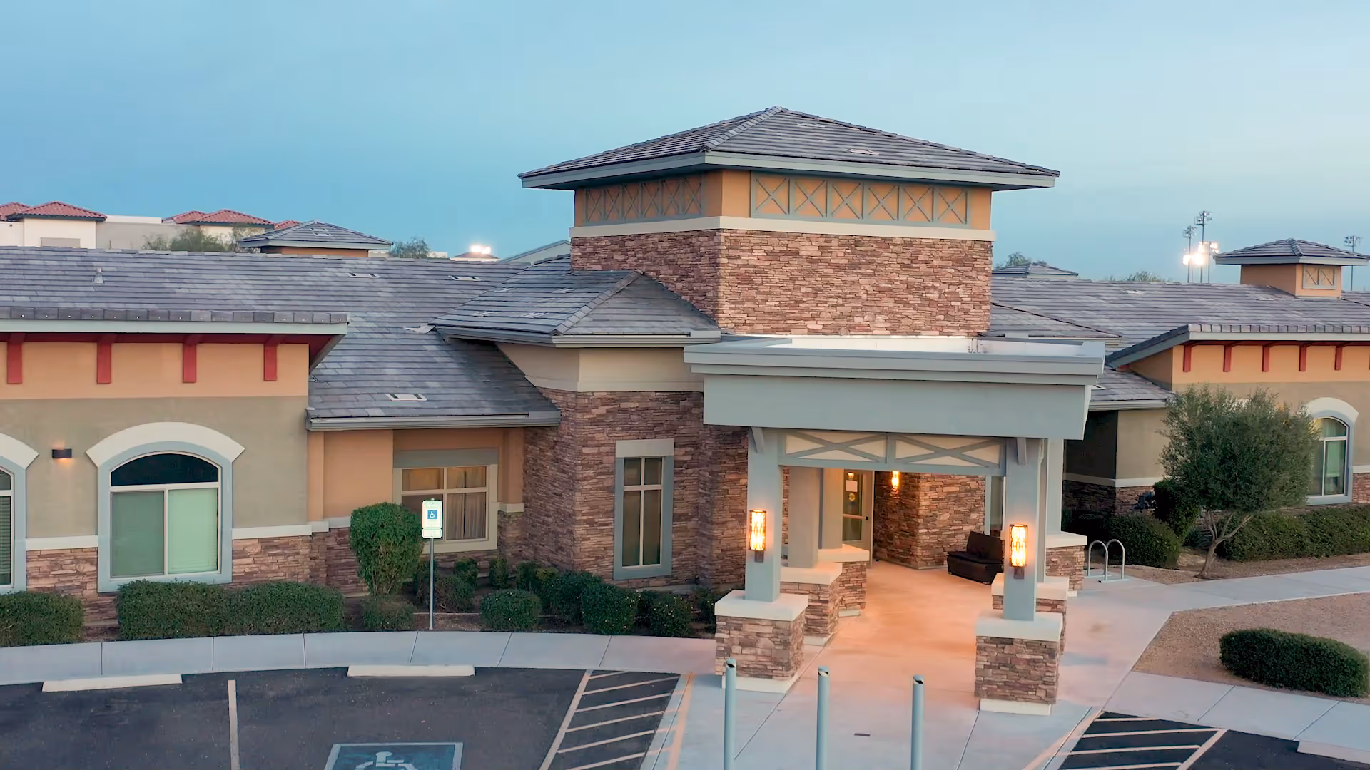 Front entrance of a single-story memory care building with stone facade, covered portico, and landscaped parking area.