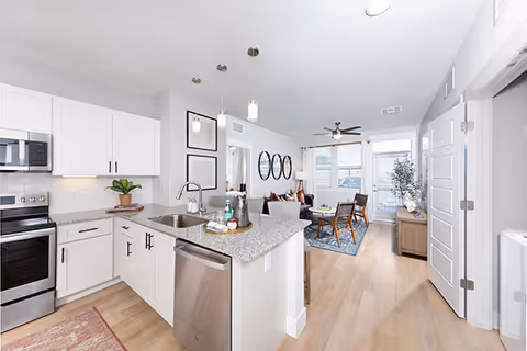 Bright open-concept kitchen with a granite island, stainless-steel appliances, and a sitting area leading into a furnished living room.
