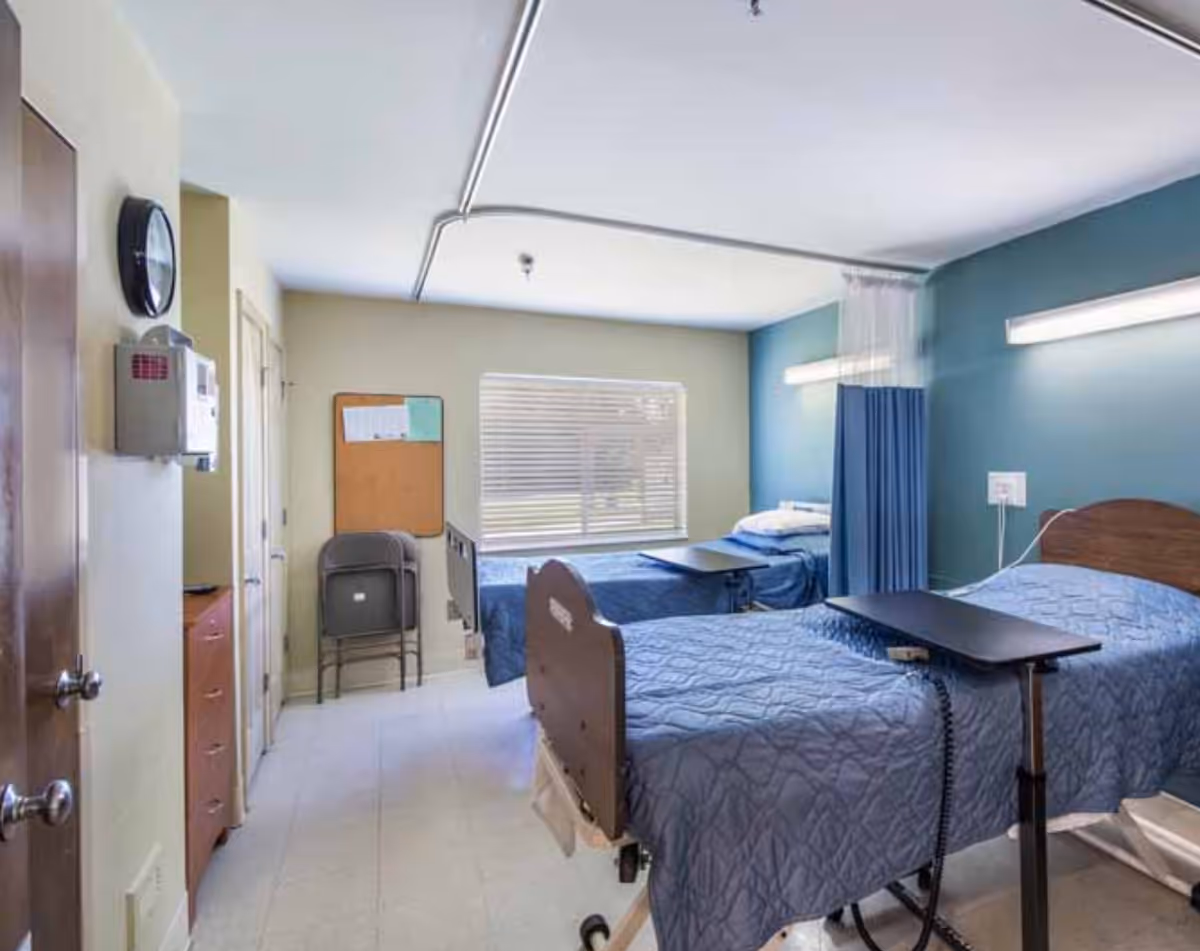 Two hospital-style beds with blue quilts in a pastel-colored patient room.