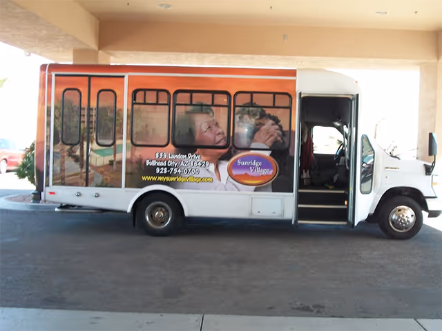 A Sunridge Village shuttle bus with promotional graphics parked under a covered drop-off area.