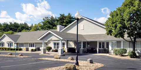 Exterior view of a senior living facility with parking lot and a covered entrance.