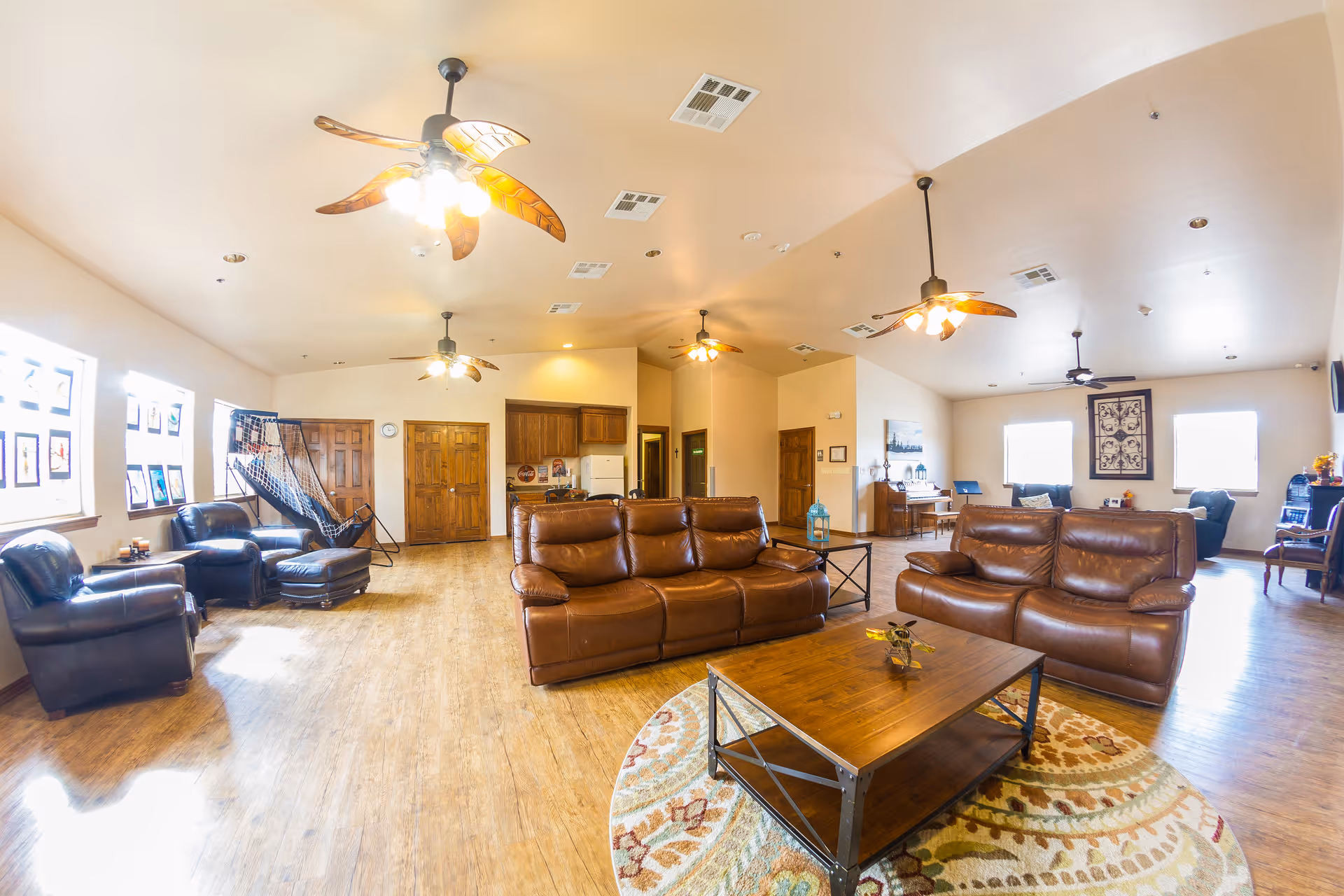 Spacious communal lounge with leather sofas, armchairs, coffee table, ceiling fans, and hardwood floors.