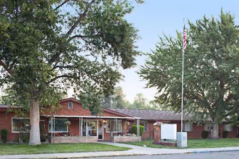 Single-story brick senior living center exterior with flagpole and mature trees.