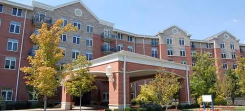 A multi-story brick senior living facility with a covered entrance and landscaped trees.