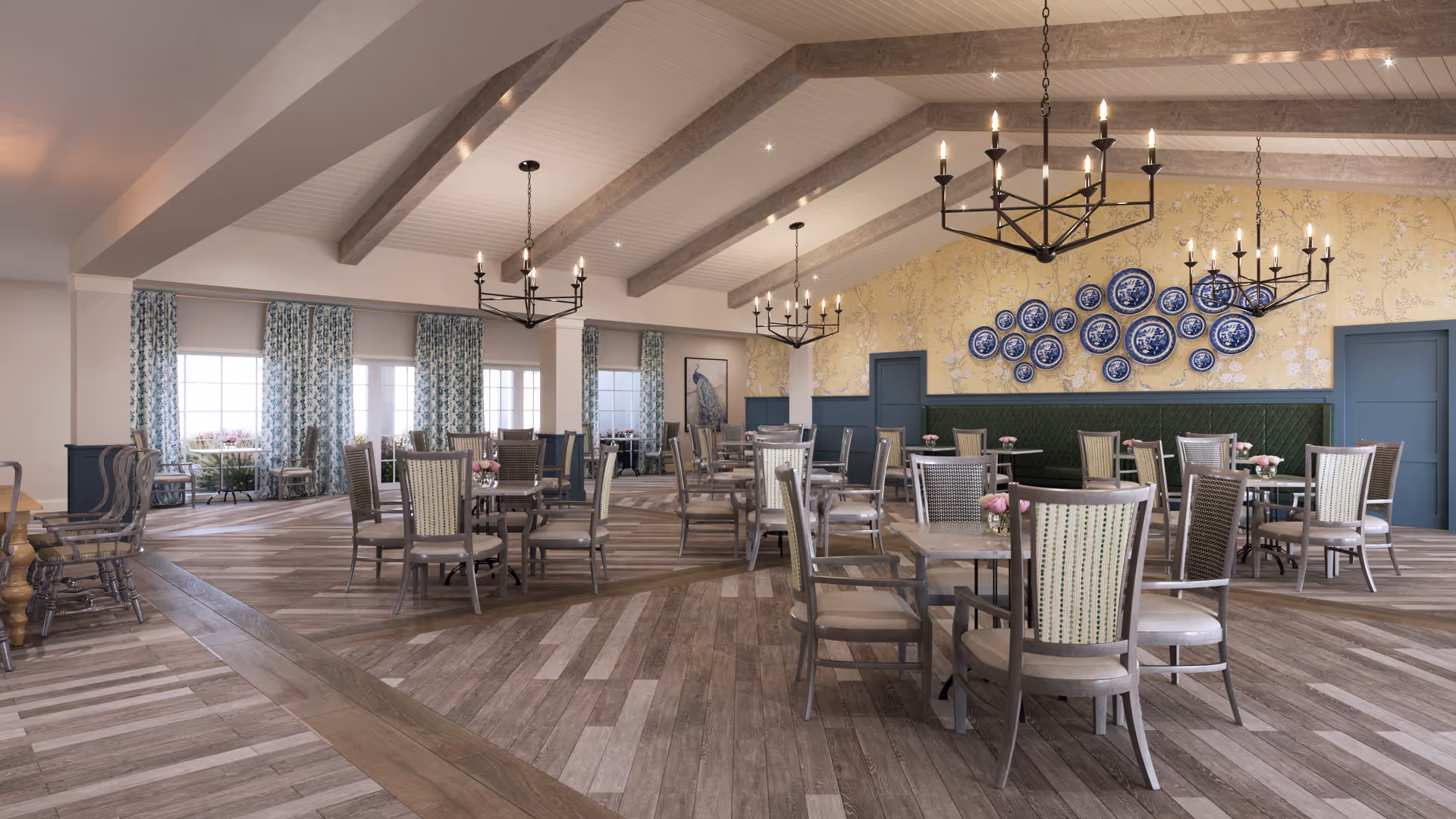 Spacious, light-filled dining room with multiple tables and chairs, hanging chandeliers, a vaulted beamed ceiling, and decorative plates on a feature wall.