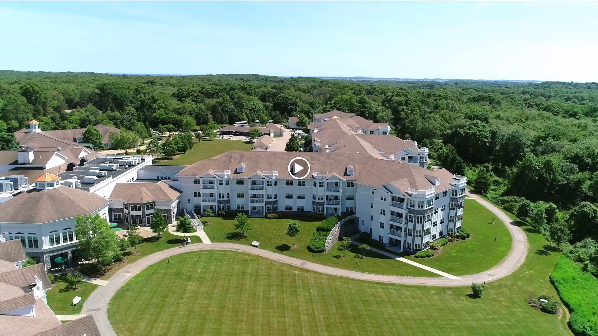 Aerial view of StoneRidge Senior Living facility showing a large multi-wing building with white exterior and brown roofs surrounded by green lawns and trees under a clear blue sky.