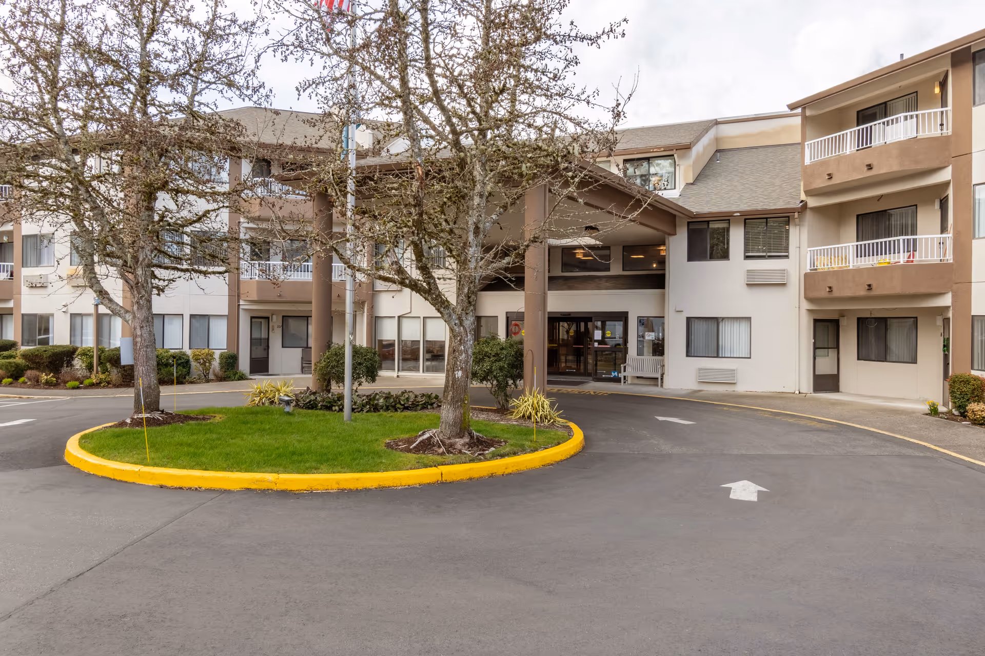 Exterior front entrance of a multi-story retirement community building with a circular driveway, trees, and balconies.