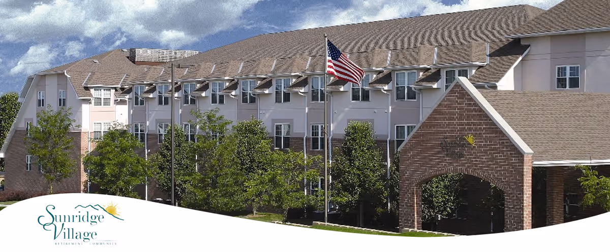 Front exterior of the Sunridge Village senior living building with an American flag, trees, and the facility logo.