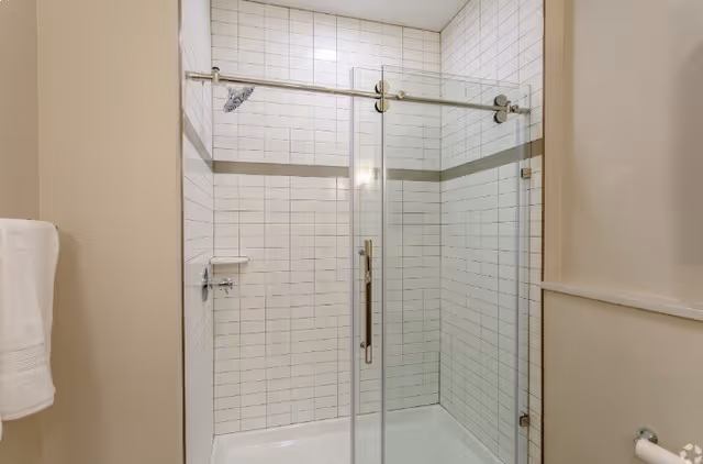 Glass-enclosed tiled shower with sliding door hardware and chrome fixtures in a bathroom.