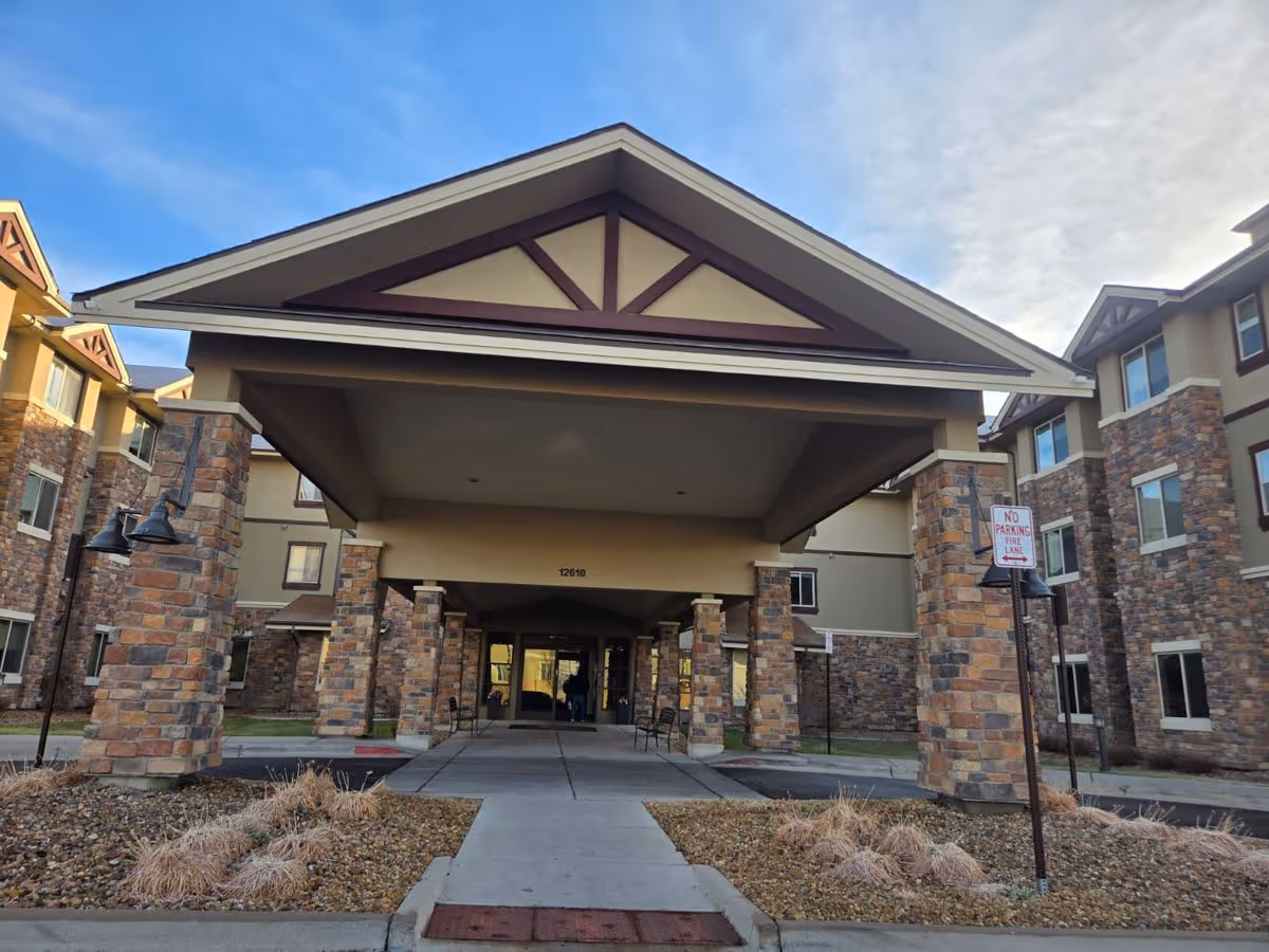 Covered entrance with stone pillars and driveway leading to the front doors of a multi-story senior living building.