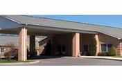 Front entrance of a brick nursing facility with a covered porte-cochère and driveway.