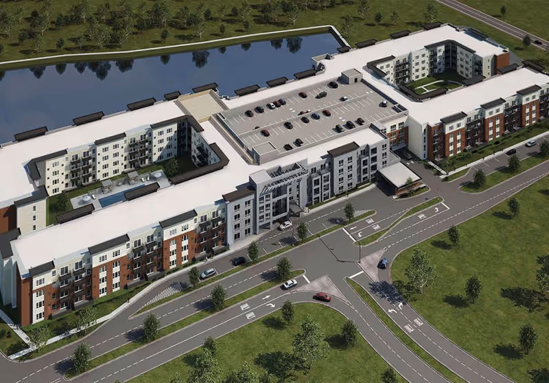 Aerial view of a large senior living facility named Lakeside Village at Oak Brook, showing a multi-story building with a rooftop parking area, surrounding roads, green lawns, and a body of water nearby.