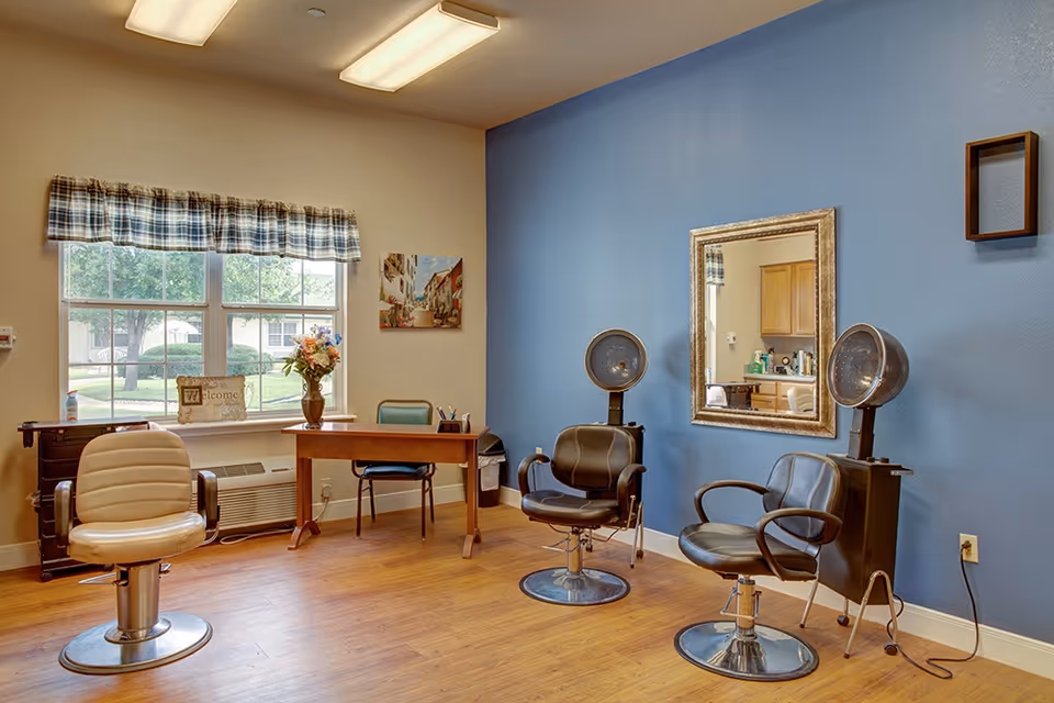 Small salon area with styling chairs and hood dryers, a desk by a window, and a mirror on a blue accent wall.