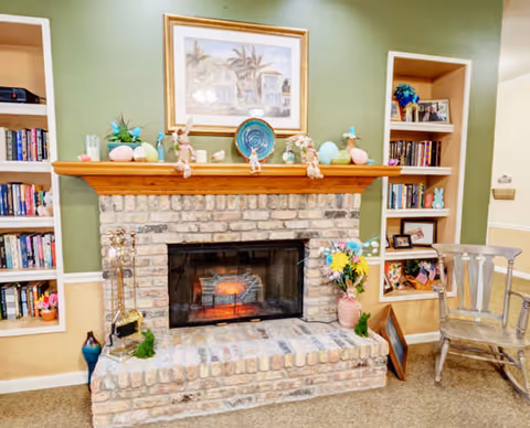 Cozy brick fireplace with a decorated mantel flanked by built-in bookshelves and a chair in a living area.
