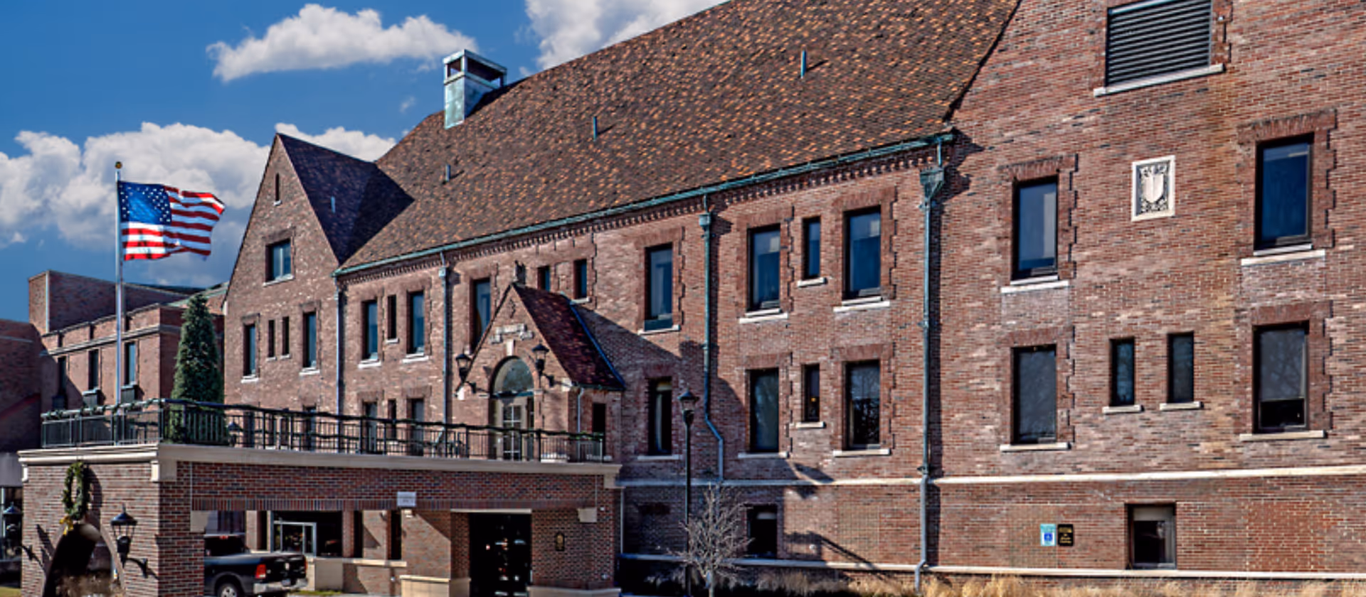 Brick senior living facility with American flag and arched entrance.