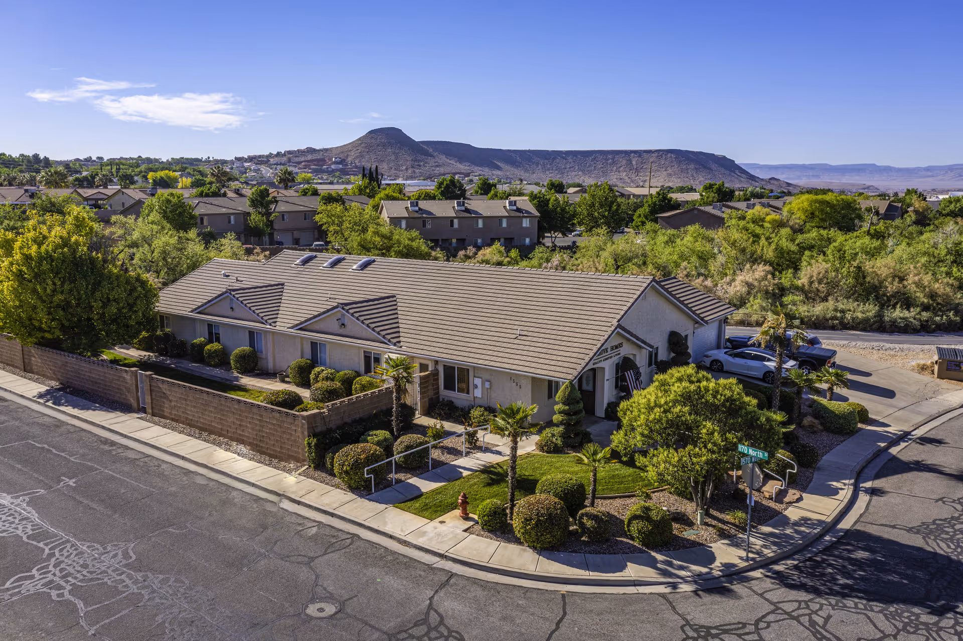 Aerial view of a single-story memory care building with landscaped grounds at a street corner and hills in the background.