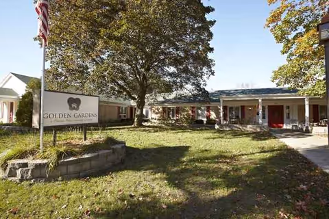 Exterior view of a single-story senior living facility with a sign, flag, and trees.