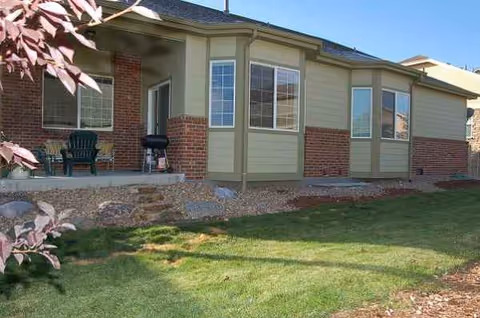 Exterior of a single-story assisted living home with a small porch and chairs.