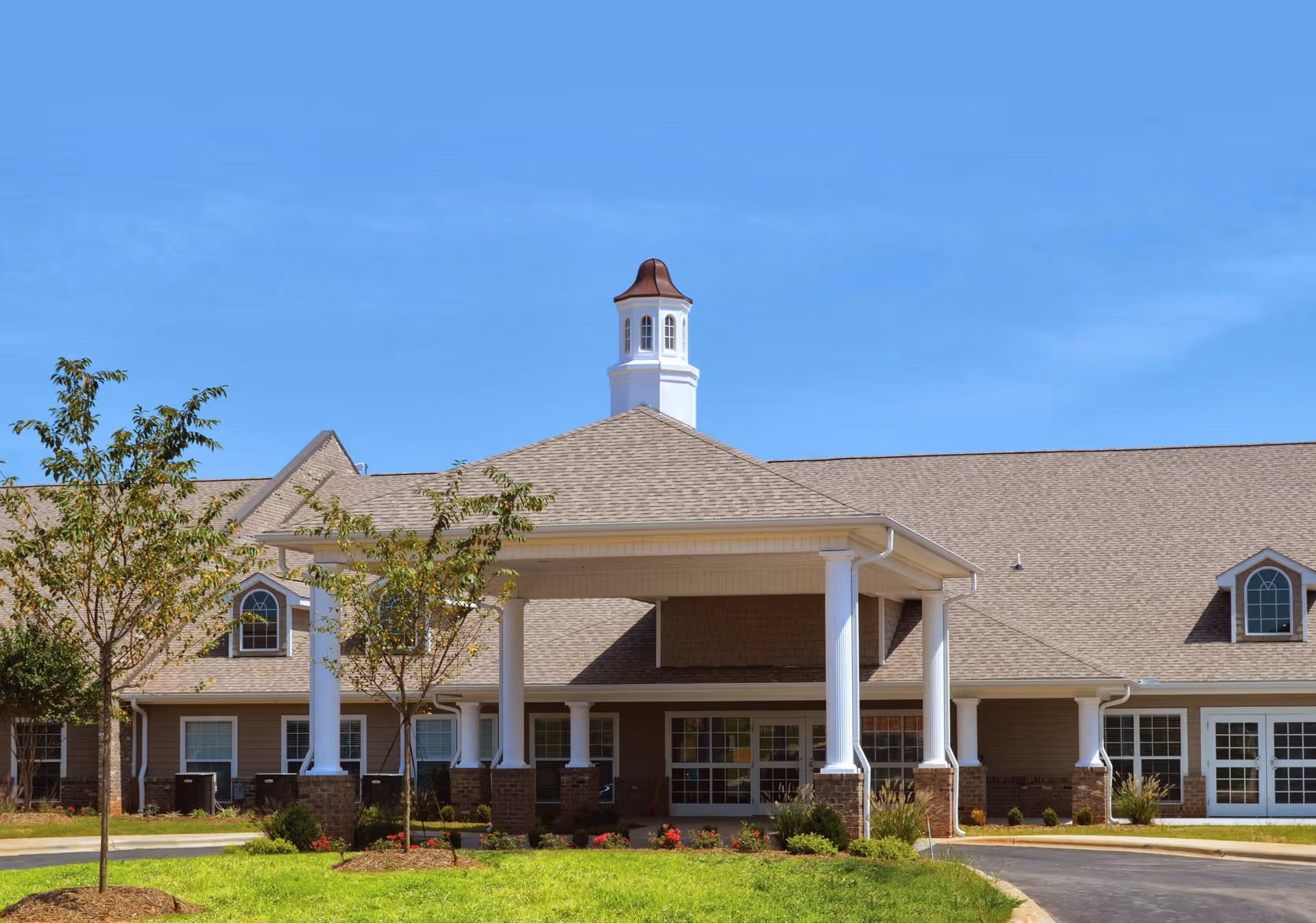 Front exterior of a single-story nursing and rehabilitation building with a covered entrance, white columns, cupola, and landscaped lawn.
