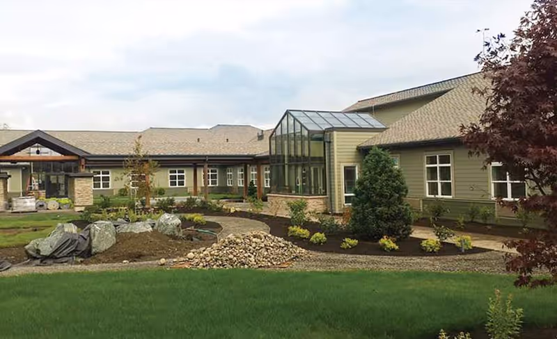 Exterior view of Silverado Bellingham Memory Care building with a landscaped courtyard and a glass sunroom.
