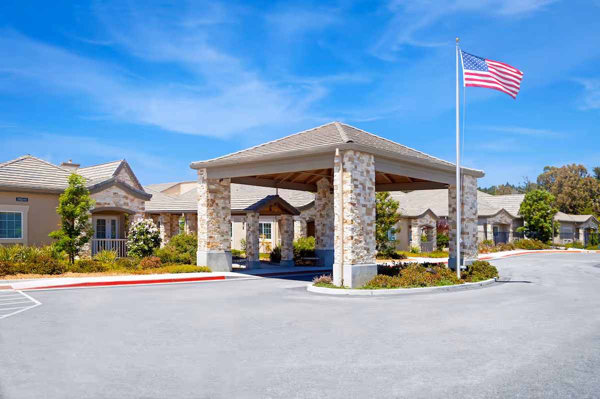 Stone porte-cochere entrance with American flag and surrounding single-story senior living buildings.