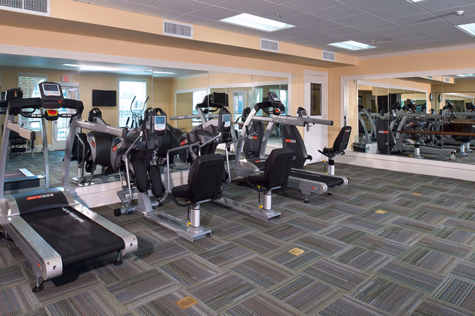 Fitness room with treadmills, recumbent bikes and large mirrors in a senior living facility.
