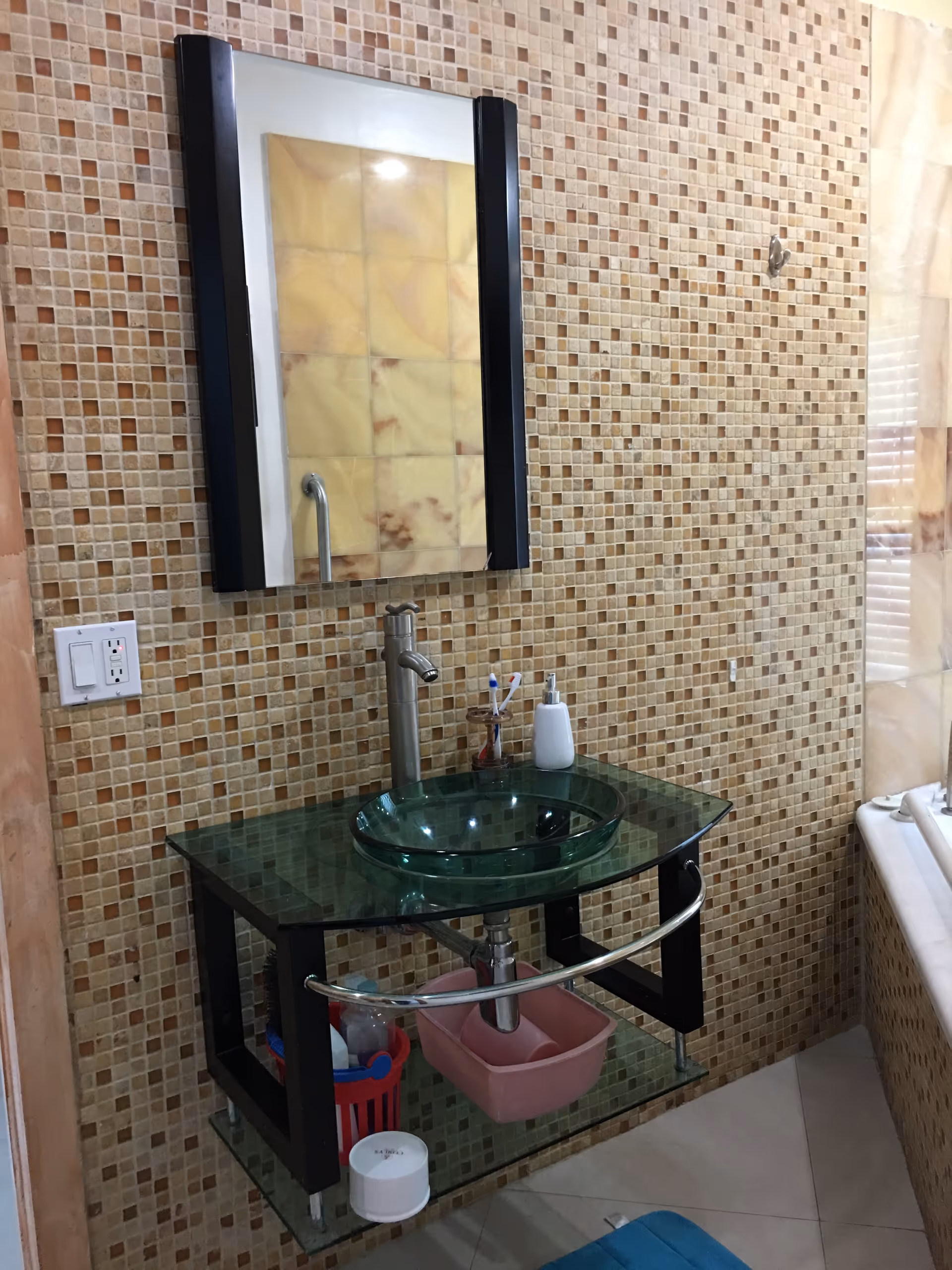 Bathroom vanity with a glass vessel sink, tall faucet, mirror, and mosaic tiled wall with a bathtub edge visible.