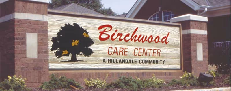 Outdoor sign for Birchwood Care Center, a Hillandale community, mounted on a brick structure with a tree logo and landscaping in front.