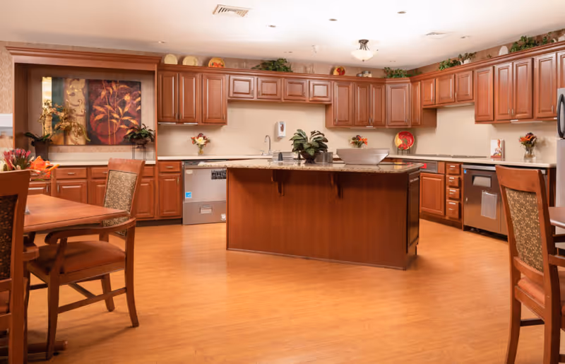 Spacious communal kitchen with a central island, wooden cabinets, countertops and dining tables with chairs.