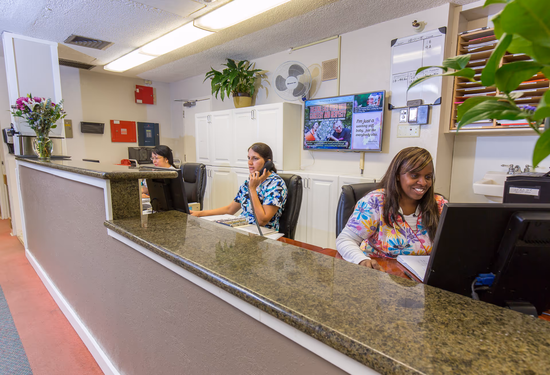 Reception desk inside a care facility with three staff members working behind a granite counter.