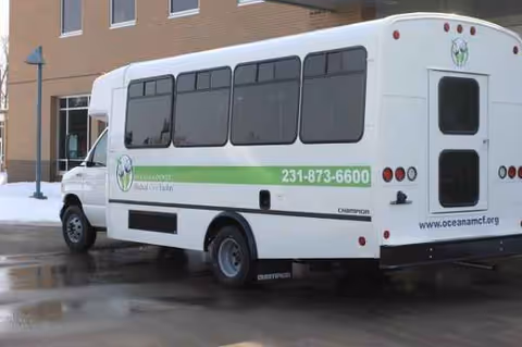 Outside Oceana Co Md Care Facility, a white shuttle bus with a green stripe.