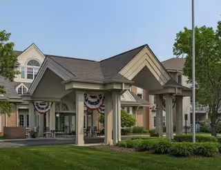 Front entrance porte-cochere of a senior living building decorated with patriotic bunting and surrounded by landscaped lawns.
